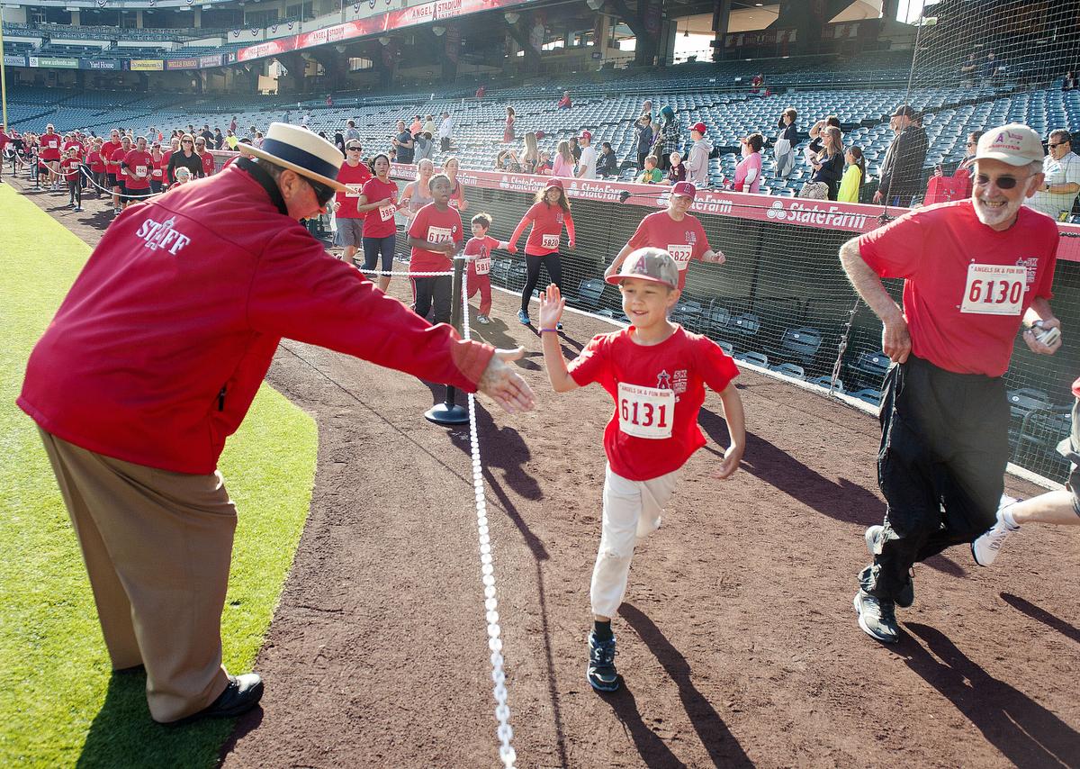 Angels usher Dave Lowell slaps skin as runners follow the course through Angels Stadium during the Angels 5K and 1 Mile Family Fun Run/Walk on Saturday, presented by St. Joseph Hoag Health, benefiting Angels Baseball Foundation. ////ADDITIONAL INFO: - 03.n.angelsrun.ks - Day: Saturday - Date: 4/11/15 - Time: 7:34:30 AM - Original file name: _KSA2690.NEF - KEN STEINHARDT, ORANGE COUNTY REGISTER --